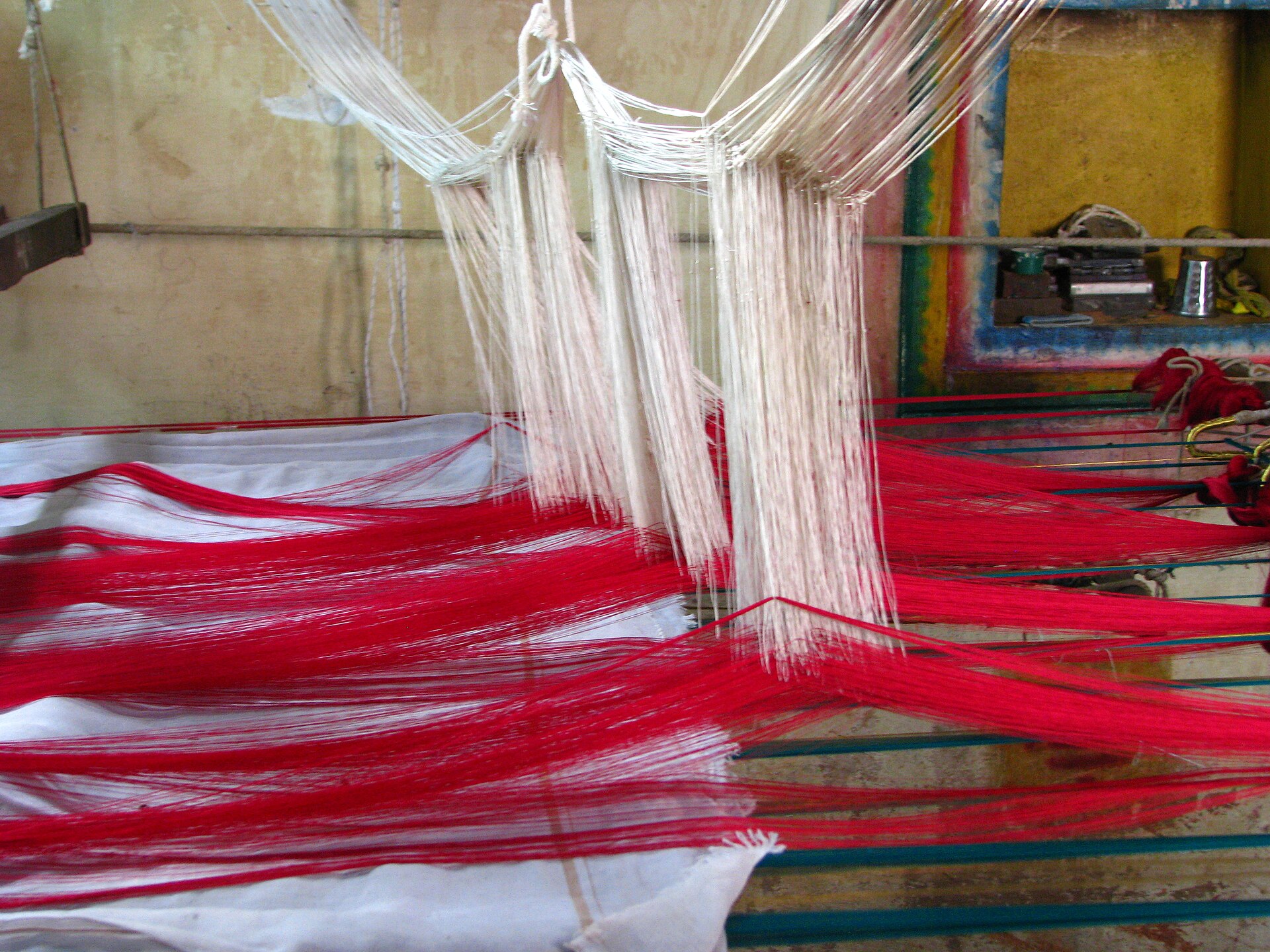 A traditional handloom weaves a vibrant red and white textile, showcasing Indian crafts.